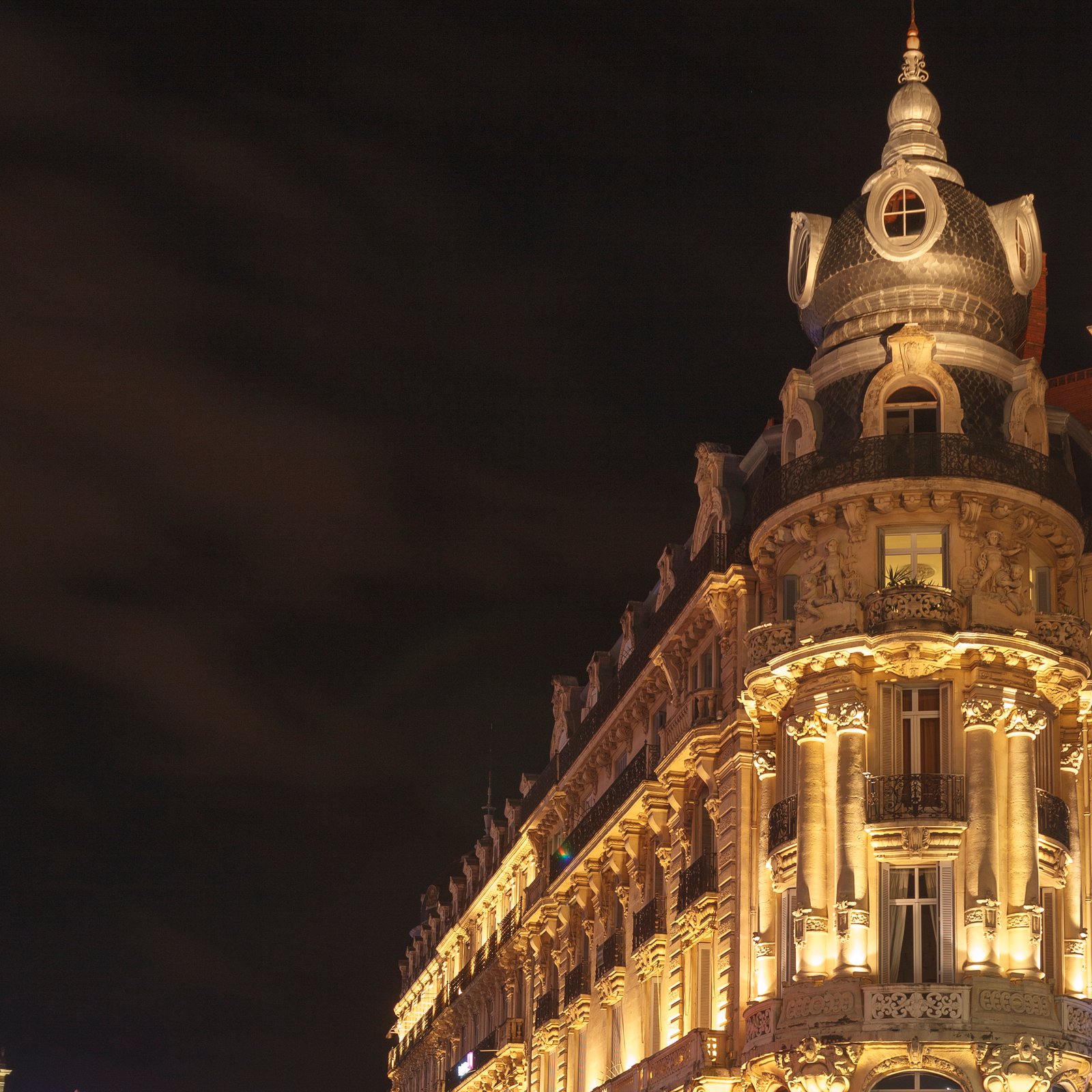 Rotonde d'un immeuble haussmannien éclairée de nuit, colonnes et dôme d'ardoise se détachant sur un ciel noir