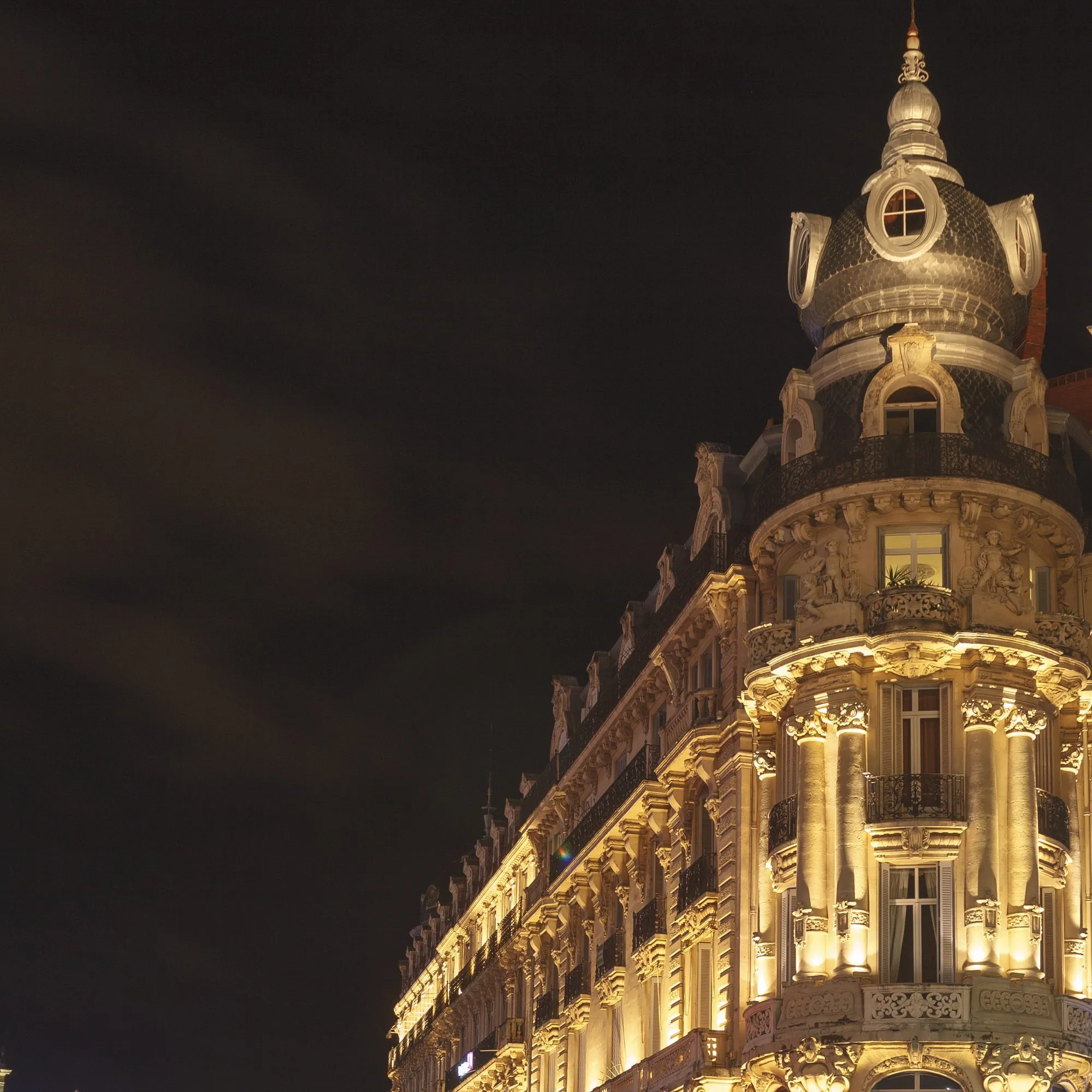 Rotonde d'un immeuble haussmannien éclairée de nuit, colonnes et dôme d'ardoise se détachant sur un ciel noir